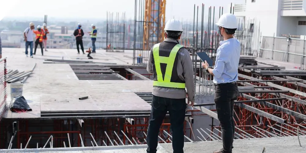 Two construction professionals in hard hats reviewing site works with a tablet on a building under construction
